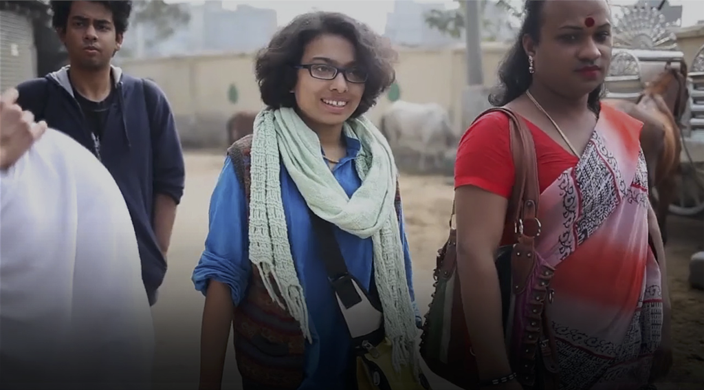 A group of individuals outdoors, including two people in colorful clothing and a smiling person with glasses and a scarf.