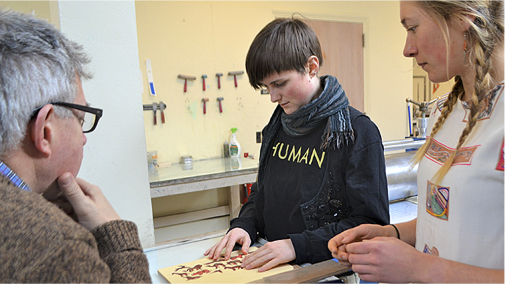 A youth and an adult work on a creative project together, engaged and focused in a workshop setting.